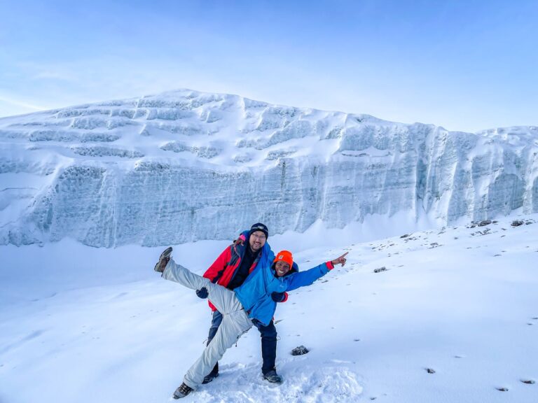 Two climbers joyfully posing on the icy glaciers of Kilimanjaro under a clear blue sky.